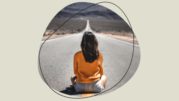 Woman sitting in the middle of the road with her back to the camera.